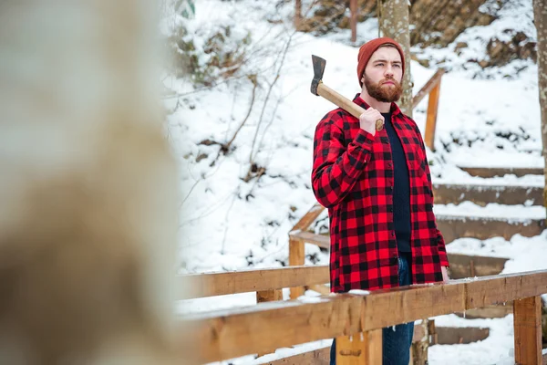 Uomo barbuto tenendo ascia e pensando nella foresta invernale — Foto Stock