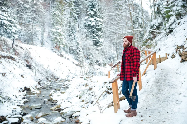 Hombre de pie cerca del río de montaña y la celebración de hacha en invierno — Foto de Stock