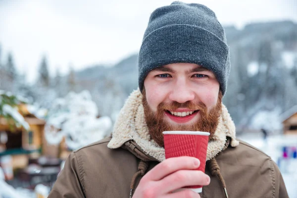 Веселый бородатый мужчина пьет горячий кофе на открытом воздухе зимой — стоковое фото