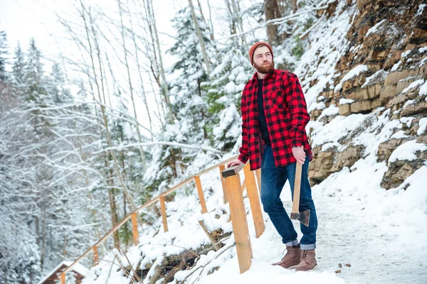 Hombre reflexivo con barba sosteniendo hacha en las montañas en invierno — Foto de Stock