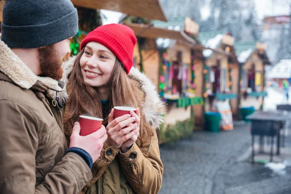 Счастливая пара пьет горячие напитки на рождественском рынке — стоковое фото