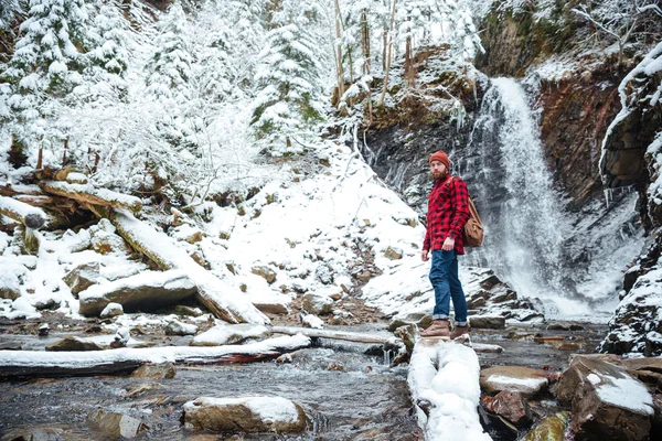 Красивый бородатый человек, идущий возле водопада в зимнем лесу — стоковое фото
