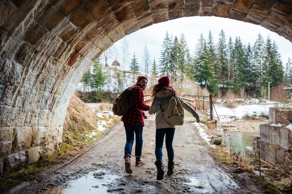 Couple holding hands and running together under the bridge — Stock Photo, Image