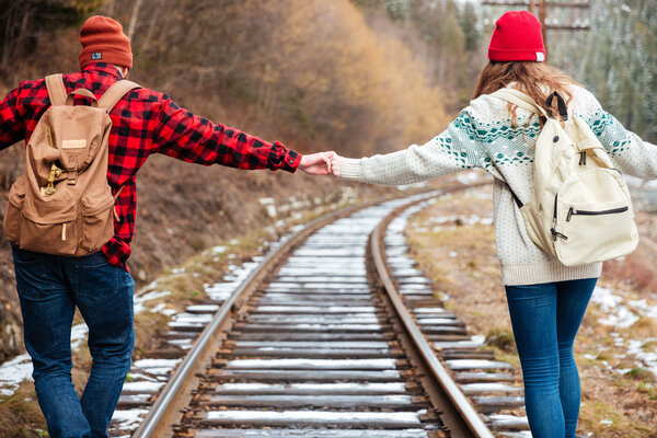 Beautiful young couple holding hands and walking along railroad together