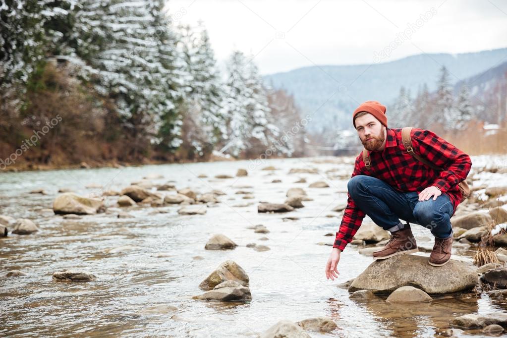 Male hiker sitting on the stone and testing wate