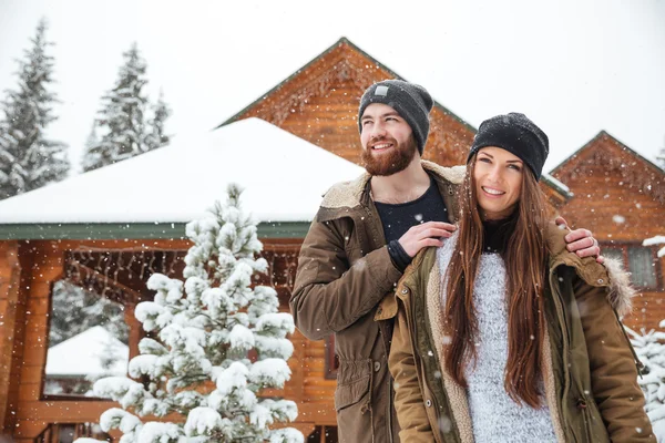 カップルの天気の雪に覆われた丸太小屋近くに立っています。 — ストック写真