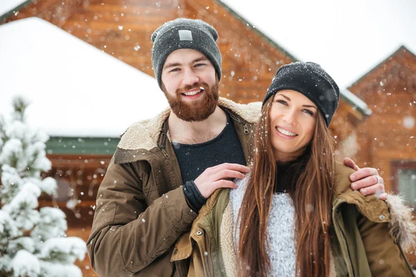 Веселая пара у деревянного коттеджа зимой — стоковое фото