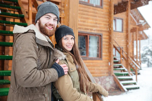 Пара стоящих рядом с деревянным коттеджем в снежную погоду — стоковое фото
