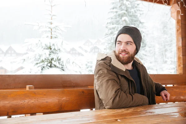 Szakállas ember ül, és mosolyogva a télen a szabadban — Stock Fotó