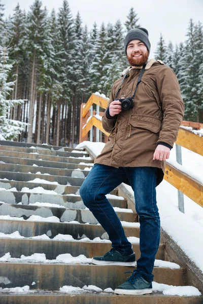 Allegro uomo in piedi e tenendo la fotocamera sulle scale in inverno — Foto Stock