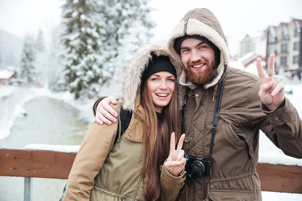 Couple avec appareil photo montrant geste de paix sur la station d'hiver — Photo