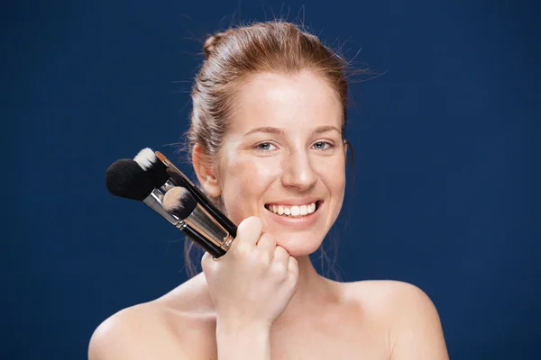 Smiling woman holding makeup brushes — Stock Photo, Image