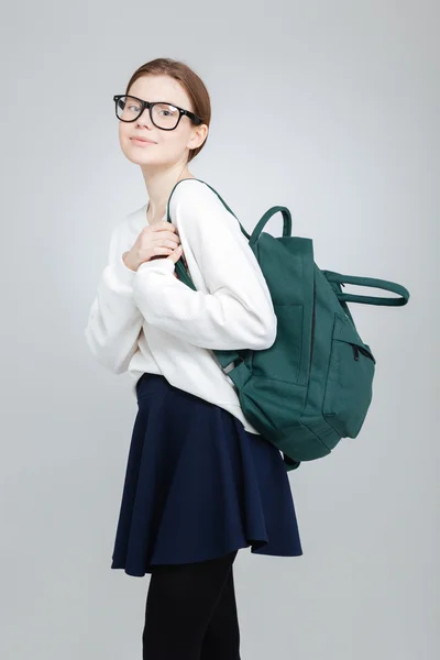 Estudante sorrindo menina em pé óculos e segurando mochila verde — Fotografia de Stock