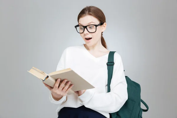 Překvapený roztomilé studentky v brýlích s batohem čtení knihy — Stock fotografie