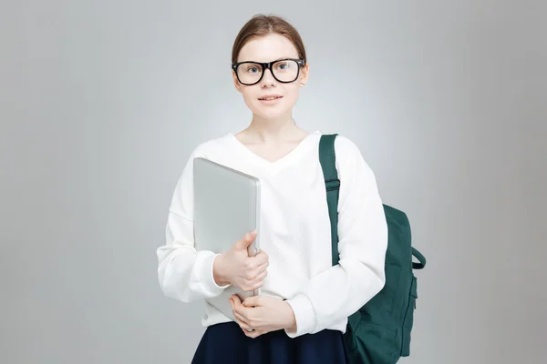 Uśmiechnięty nastoletnia dziewczyna w okularach gospodarstwa zielony plecak i laptopa — Zdjęcie stockowe