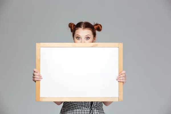Funny lovely young woman hiding behind  blank whiteboard — Stock Photo, Image