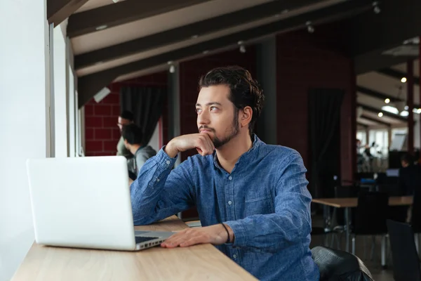 Fundersam man sitter vid bordet med laptop — Stockfoto