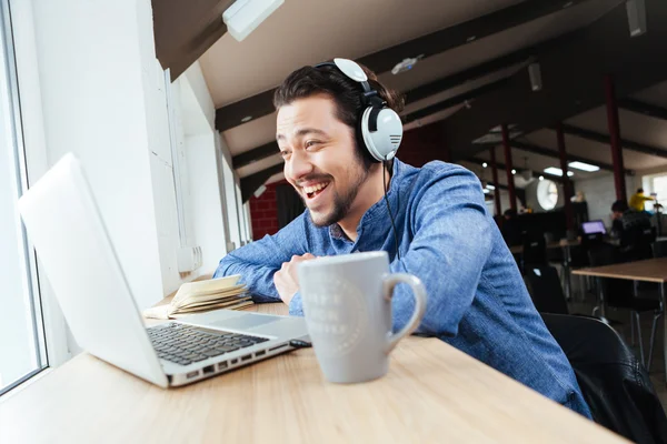 Hombre alegre en auriculares usando el ordenador portátil — Foto de Stock