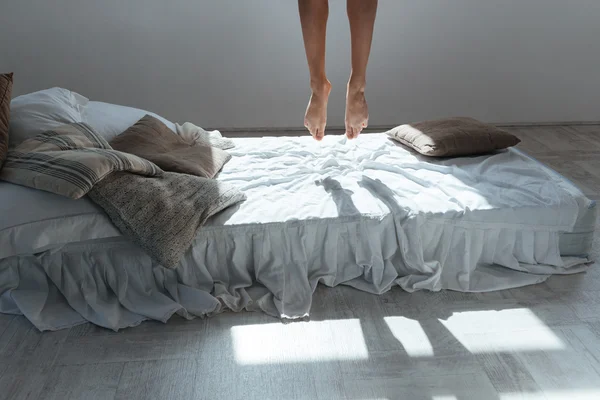 Slim legs of young woman flying in air above bed — Stock Photo, Image