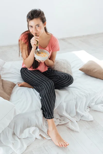 Mujer bonita en pijama comiendo cereales con leche en la cama —  Fotos de Stock