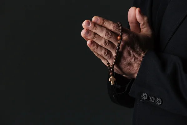 Manos del sacerdote sosteniendo el rosario y rezando — Foto de Stock