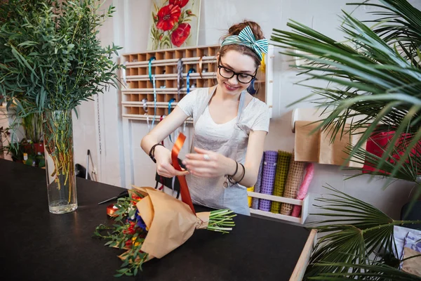 Smiling woman florist making bouquet of flowers with red ribbon — Stock Photo, Image