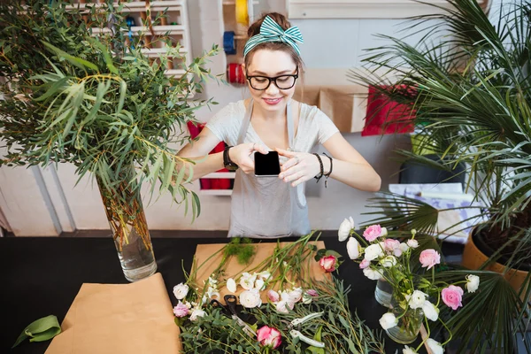 Gelukkige vrouw nemen van foto's van bloemen op tafel in de winkel — Stockfoto