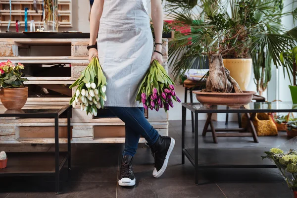 Vrouw bloemist in schort en sneakers met twee tulpen boeketten — Stockfoto