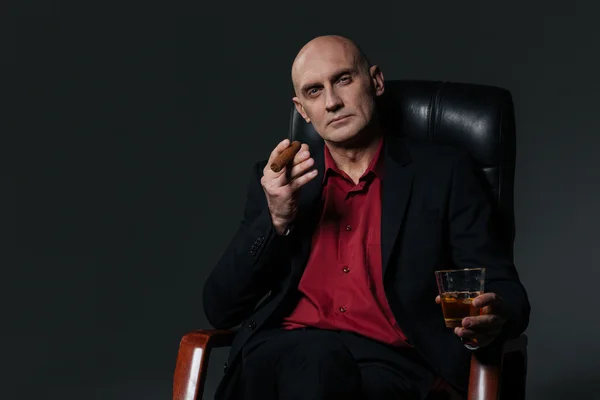Sério bonito empresário beber uísque e fumar charuto sentado — Fotografia de Stock