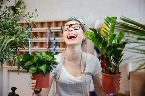 Happy woman florist holding plants in flowerpots and laughing
