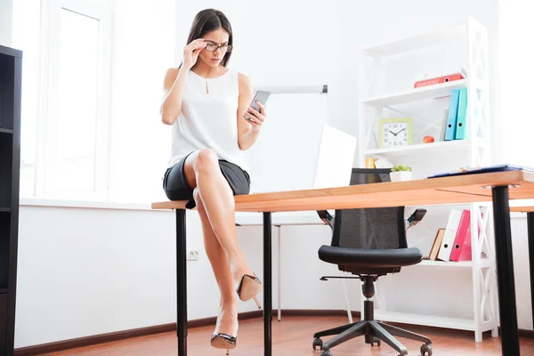 Zakenvrouw zittend op de tafel en het gebruik van smartphone — Stockfoto