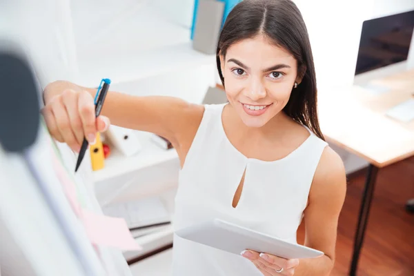 Businesswoman holding tablet computer and writing on whiteboard — Stock Photo, Image