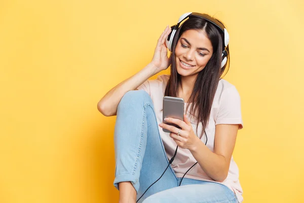 Женщина слушает музыку в наушниках и использует смартфон — стоковое фото