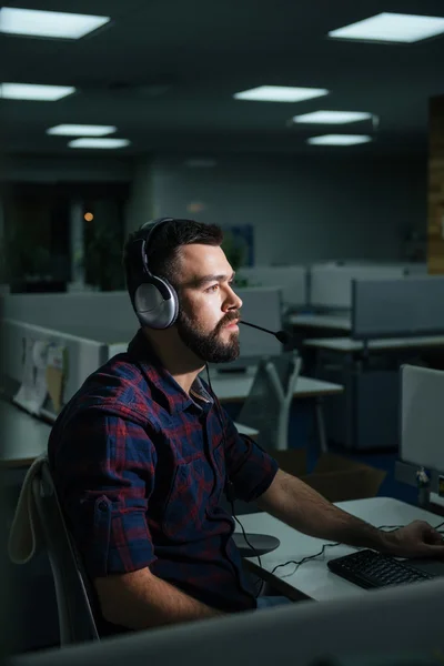 Homem de negócios sério em fones de ouvido trabalhando no escritório tarde — Fotografia de Stock