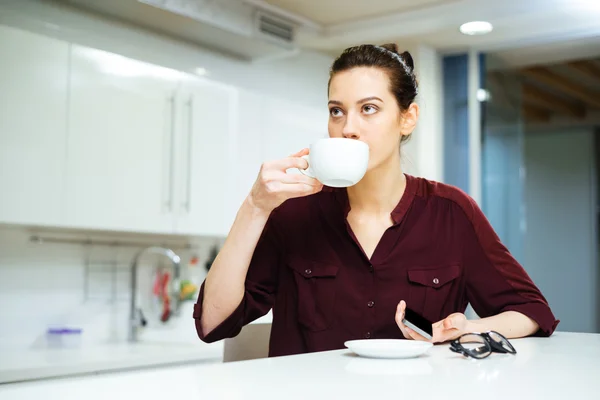 座っていると台所でコーヒーを飲む女性 — ストック写真