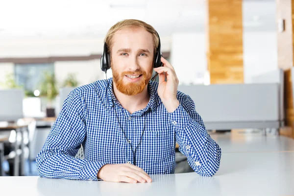 Glimlachende man zittend op de werkplek en het gebruik van de hoofdtelefoon — Stockfoto
