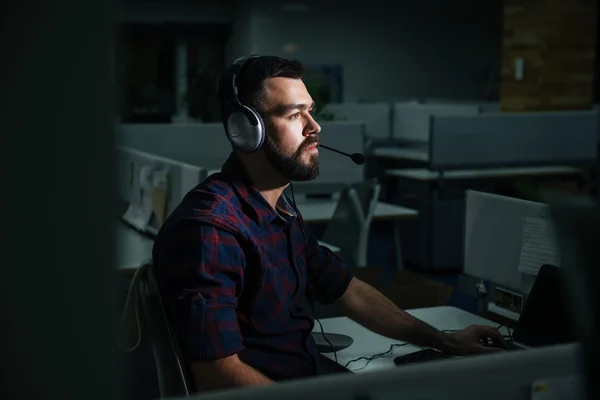 夜の暗いオフィスで働いているヘッドフォンに男を集中してください。 — ストック写真