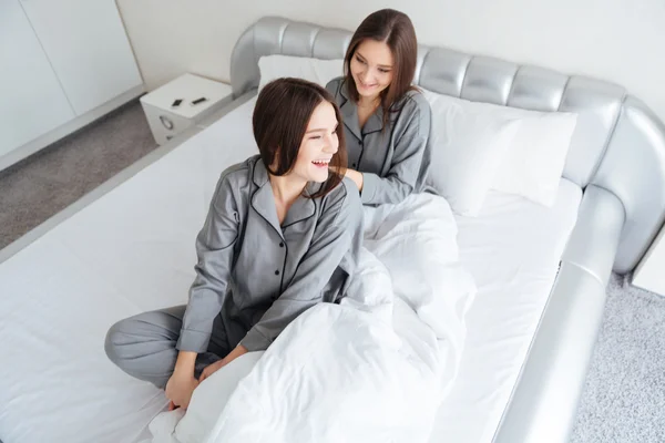 Two happy sisters twins sitting on bed and laughing — Stock Photo, Image