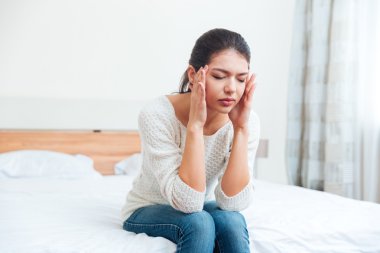 Baş ağrısı ile yatağın üstüne oturan kadın
