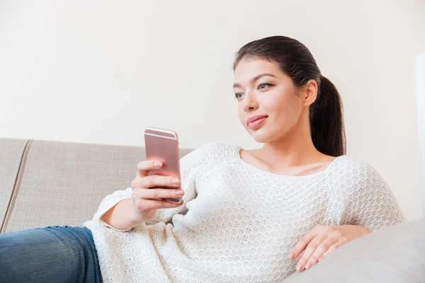 Женщина лежит на диване и пользуется смартфоном — стоковое фото