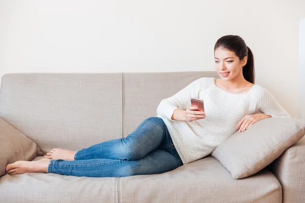 Mujer acostada en el sofá y usando smartphone —  Fotos de Stock