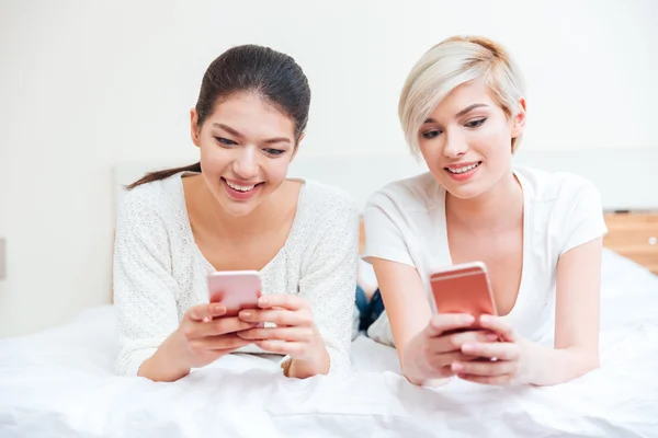 Mujeres acostadas en la cama y usando teléfonos inteligentes — Foto de Stock
