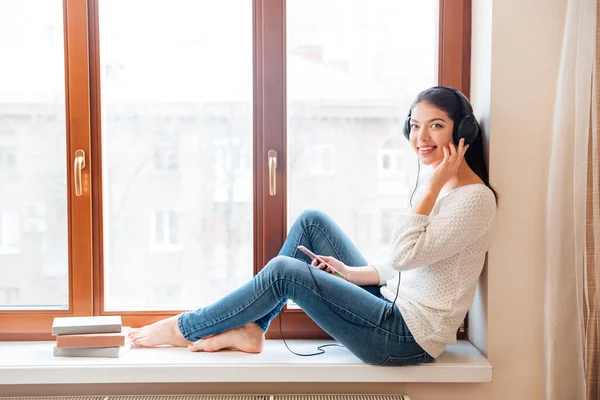 Femme heureuse assise sur le rebord de la fenêtre avec écouteurs — Photo