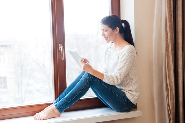 Femme assise sur le rebord de la fenêtre et utilisant un ordinateur tablette — Photo