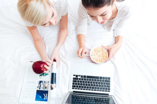 Две женщины лежат на кровати и используют ноутбук — стоковое фото