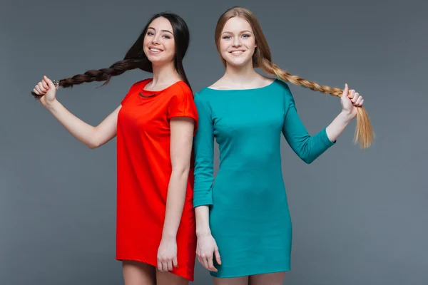 Две улыбающиеся красивые женщины стоят и показывают свои длинные косы — стоковое фото