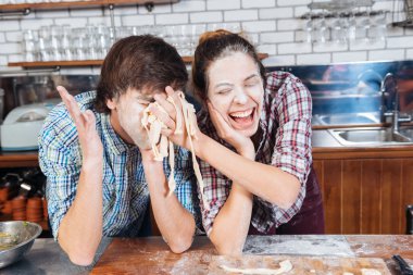 Funny couple with flour on faces having fun using dough clipart