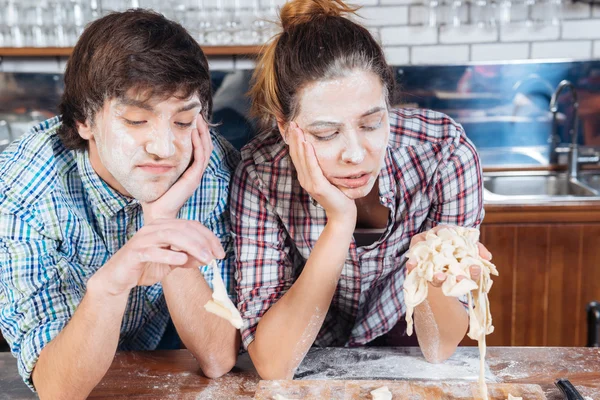 Triste pareja aburrida con harina en las caras amasando masa — Foto de Stock