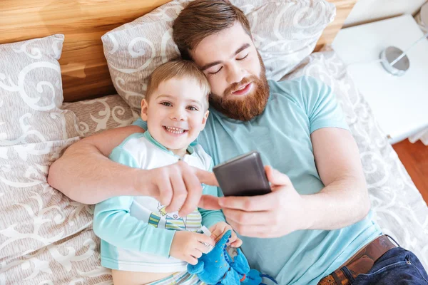 Vater und Sohn benutzen Handy gemeinsam im Bett — Stockfoto