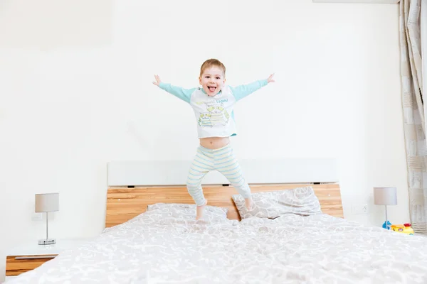 Веселый маленький мальчик, показывающий язык и прыгающий на кровати — стоковое фото